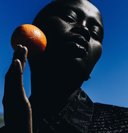 Woman holding an orange beside her cheek